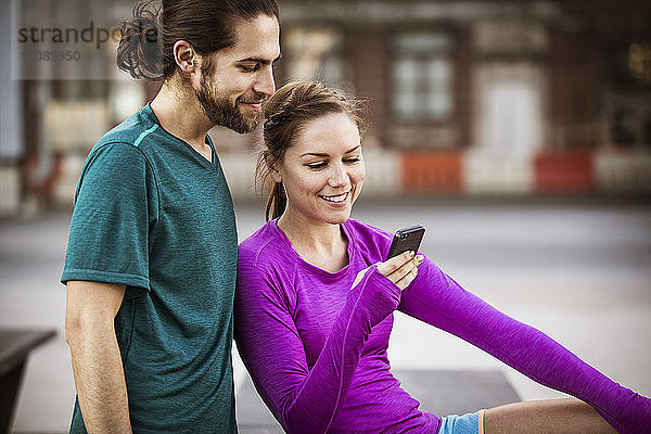 Glückliche Frau zeigt einem Freund ihr Handy  während sie auf einer Bank sitzt