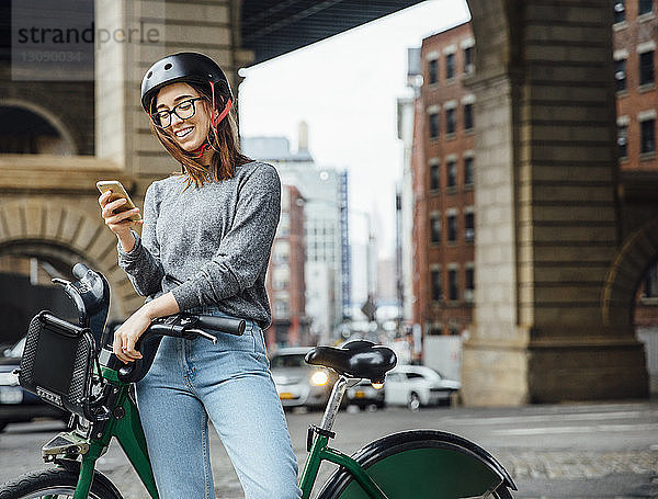 Glückliche Frau benutzt Smartphone  während sie mit dem Fahrrad auf der Straße steht