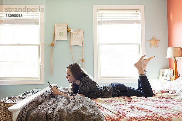 Seitenansicht einer Frau  die ein Mobiltelefon benutzt  während sie zu Hause im Bett liegt