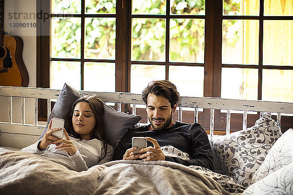 Ehepaar benutzt Smartphones  während es zu Hause im Bett liegt
