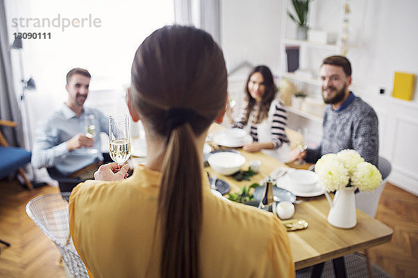 Rückansicht einer Frau  die Champagnerflöte hält  während Freunde am Tisch sitzen