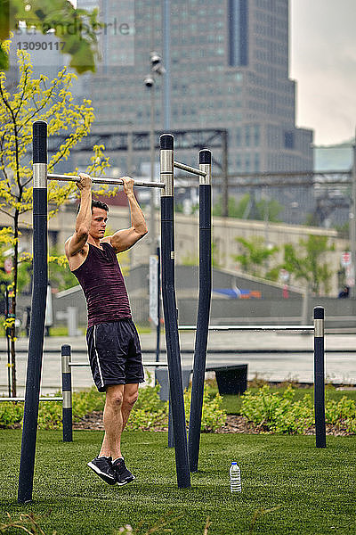 Ein junger Mann in voller Länge hält beim Turnen im Stadtpark eine Gymnastikstange