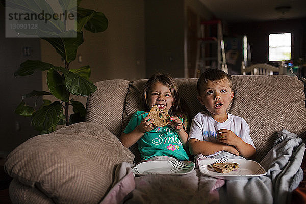 Glückliche Geschwister essen Brot auf dem Sofa