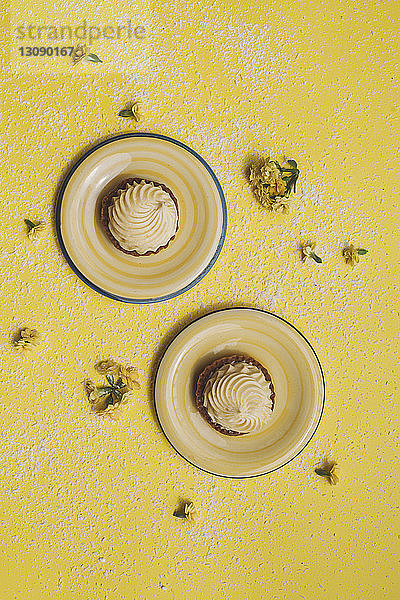 Draufsicht auf Muffins in Tellern mit Blumen auf gelbem Hintergrund