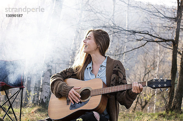 Fröhliche Frau spielt Gitarre im Wald