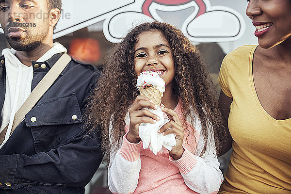 Porträt eines Mädchens  das Eiswaffeln hält  während es mit den Eltern zusammensitzt