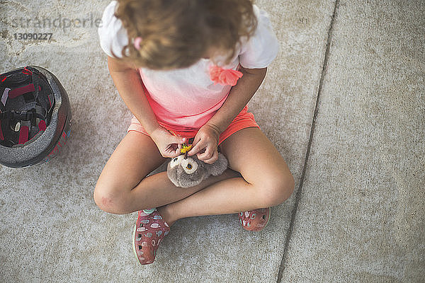 Hochwinkelansicht eines auf dem Boden sitzenden Mädchens  das mit einem Spielzeug spielt