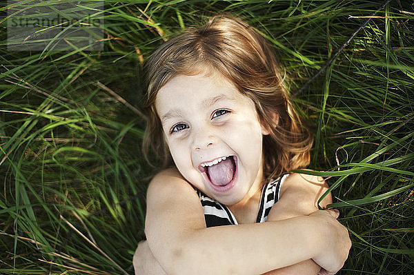 Hochwinkelporträt eines glücklichen Mädchens  das auf einem Grasfeld im Park liegt