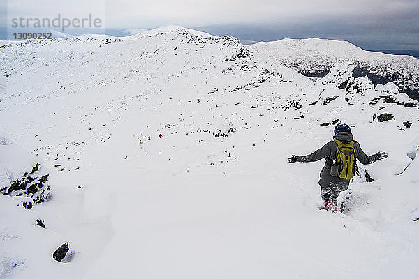 Rückansicht eines Wanderers  der auf einem schneebedeckten Berg gegen den Himmel läuft