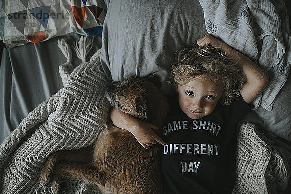 Bildnis eines Jungen mit Hund auf dem Bett liegend