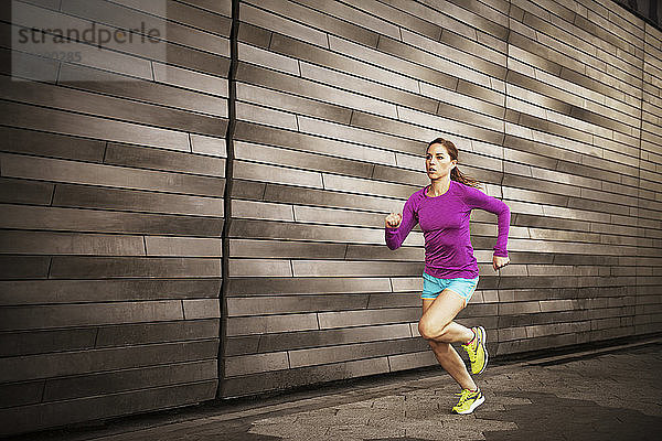 Frau joggt auf Bürgersteig an Wand