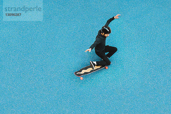 Hochwinkelaufnahme eines Mannes beim Skateboardfahren auf blauem Boden im Skateboard-Park