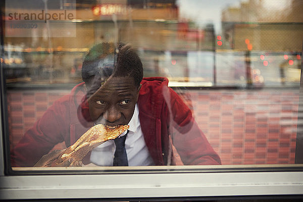 Student isst Pizza durch Fenster mit Spiegelung der Stadt