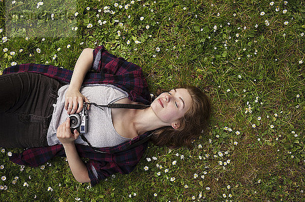 Draufsicht einer Frau  die eine Kamera hält  während sie sich auf dem Rasen eines Parks entspannt
