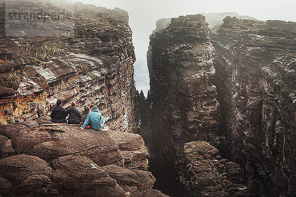 Rückansicht von Freunden  die auf einer Felsklippe sitzen