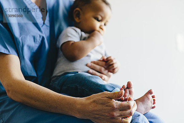 Mittelteil einer Ärztin  die einen kleinen Jungen hält  während sie vor weißem Hintergrund sitzt