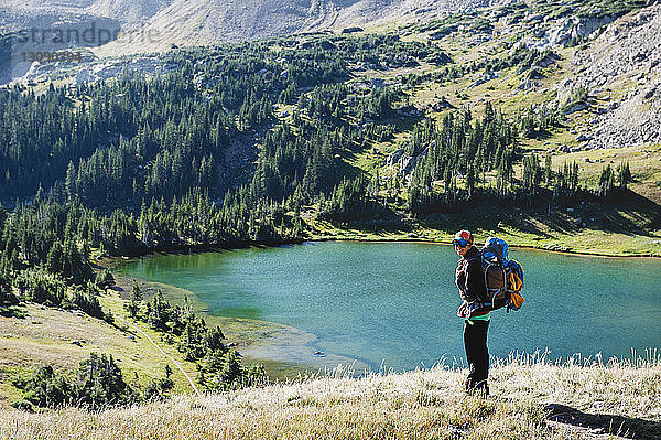 Lächelnde Frau mit Rucksack steht am See im Berg