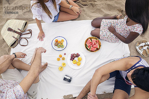 Draufsicht auf Freunde  die am Strand sitzend Früchte essen