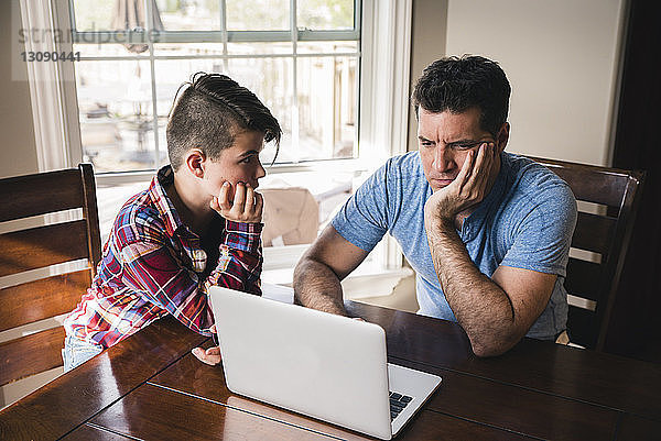 Sohn sieht gestressten Vater an  der zu Hause einen Laptop benutzt