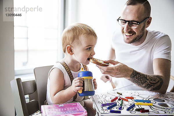 Lächelnder Vater füttert niedliche Tochter beim Zeichnen am Tisch