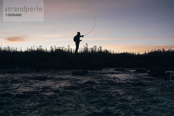 Silhouette eines Mannes  der bei Sonnenuntergang gegen den Himmel fischt