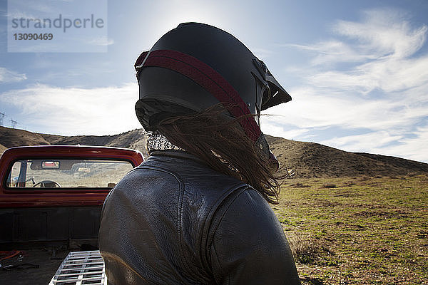 Rückansicht einer Motorradfahrerin mit Helm am Pick-up auf einem Berg gegen den Himmel