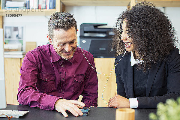 Glückliche Geschäftsleute  die am Tisch im Büro ein Mobiltelefon benutzen