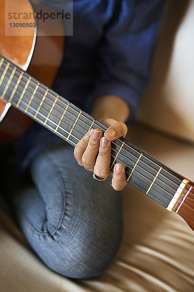 Ausgeschnittenes Bild einer Frau  die zu Hause auf dem Sofa sitzt und Gitarre übt