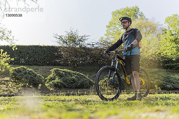 Junger Mann in voller Länge mit Mountainbike auf dem Feld im Park stehend