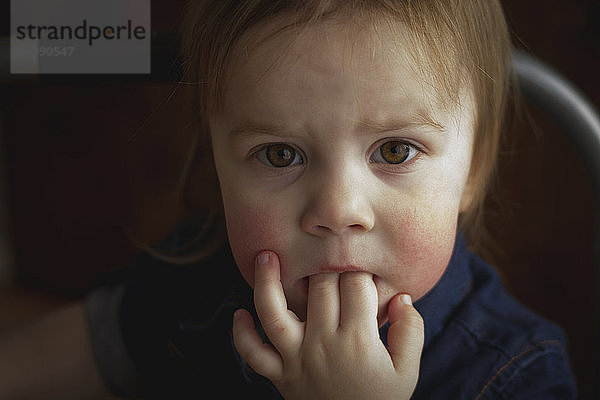 Nahaufnahme-Porträt eines süßen Mädchens mit Fingern im Mund zu Hause