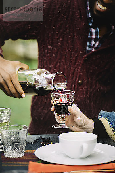 Mitschnitt eines Mannes  der am Tisch sitzend für einen Freund Wein in einem Glas einschenkt