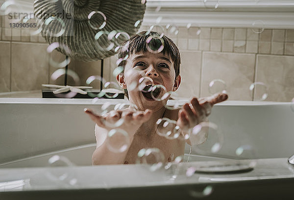 Fröhlicher Junge spielt mit Seifenblasen beim Baden in der Badewanne