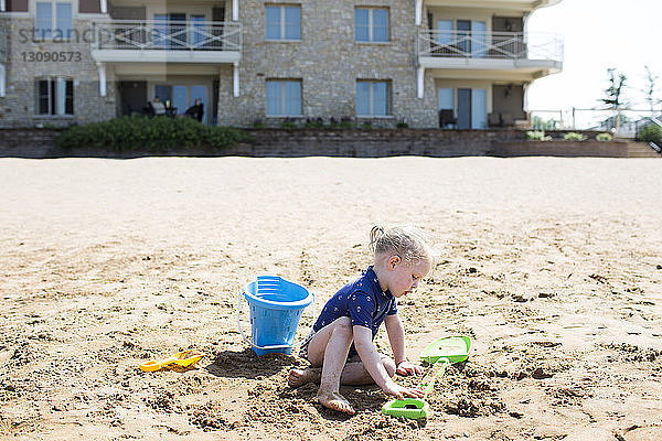 Mädchen spielt mit Spielzeug am Sandstrand an einem sonnigen Tag
