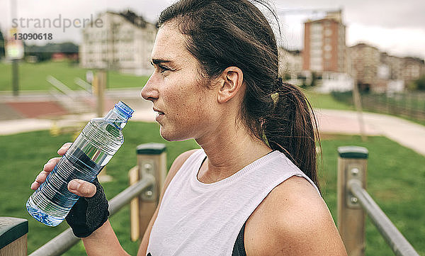 Frau schaut weg  während sie eine Wasserflasche im Park hält