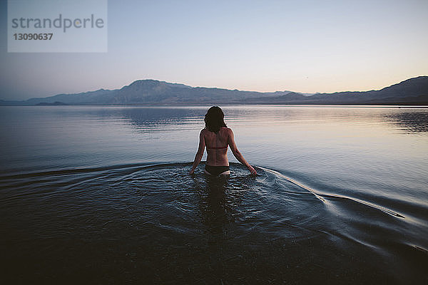 Rückansicht einer Frau im Bikini  die in der Dämmerung im See vor klarem Himmel steht