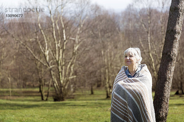 Nachdenkliche ältere Frau in eine Decke gehüllt  die im Winter auf dem Feld steht