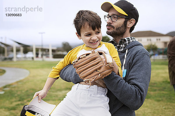 Vater trägt glücklichen Sohn im Stehen auf Sportplatz