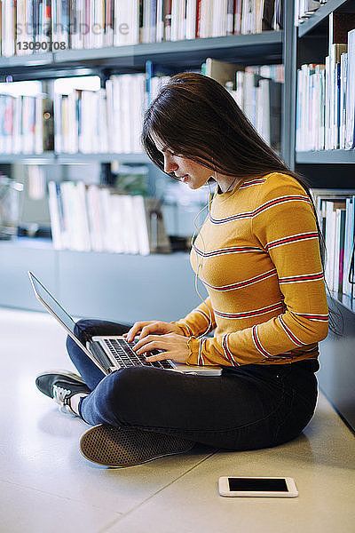 Seitenansicht einer Frau  die einen Laptop-Computer benutzt  während sie in der Bibliothek auf dem Boden sitzt