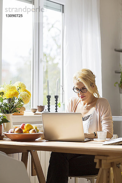Frau benutzt Laptop-Computer  während sie am Tisch am Fenster sitzt