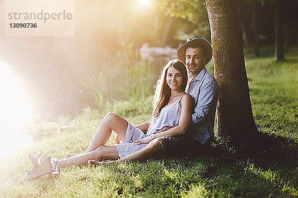 Porträt eines Paares  das auf einem Grasfeld bei einem Baum im Park sitzt