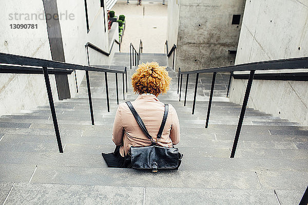 Rückansicht einer auf Stufen sitzenden Frau mit Tasche