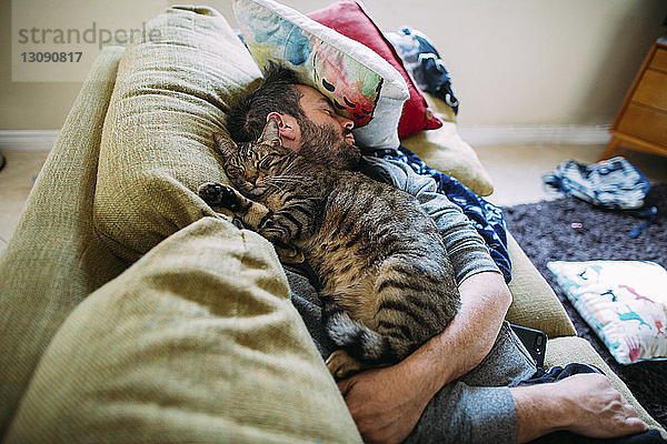 Hochwinkelansicht eines Mannes mit Katze  der zu Hause auf dem Sofa schläft