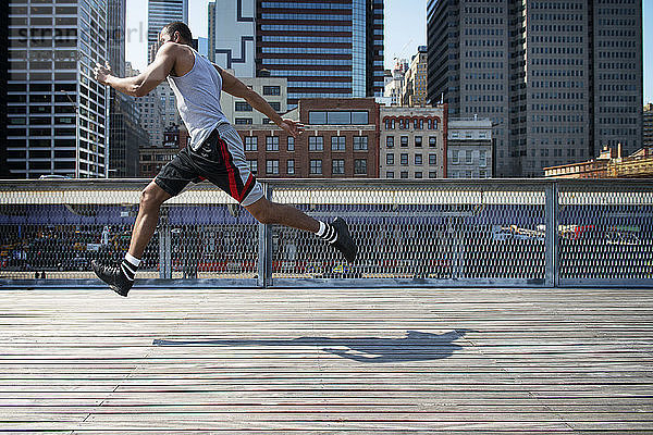 Seitenansicht eines Mannes  der auf einer Promenade gegen moderne Gebäude springt