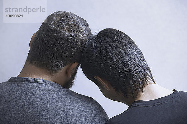 Rückansicht eines schwulen Paares  das sich zu Hause an einer weißen Wand entspannt