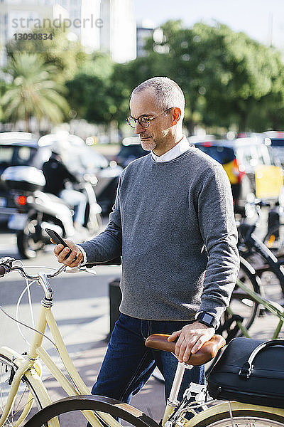 Geschäftsmann benutzt Smartphone  während er in der Stadt mit dem Fahrrad steht