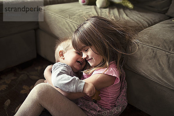 Glückliches Mädchen umarmt Bruder am Sofa im Wohnzimmer
