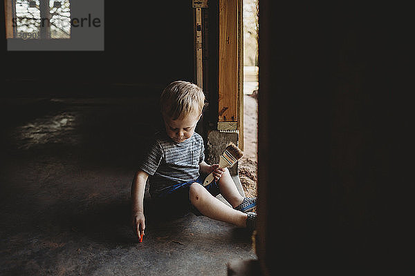Kleiner Junge mit Bürste sitzt am Eingang in einem verlassenen Raum