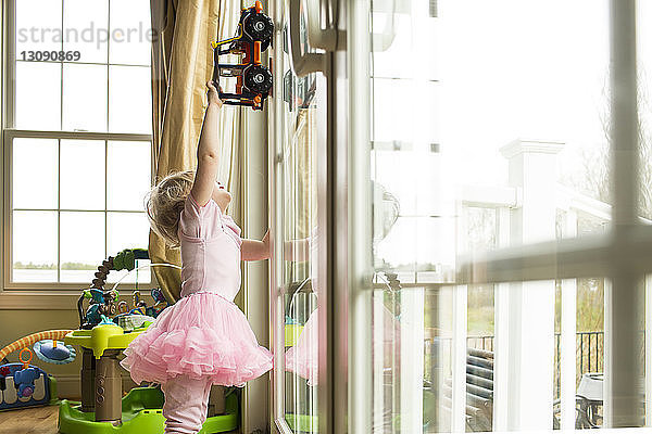 Mädchen spielt zu Hause mit Spielzeugauto am Fenster