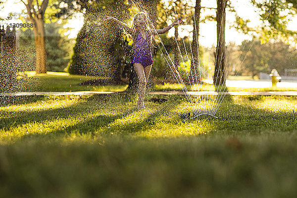 Glückliches Mädchen spielt im Sprinkler im Hinterhof