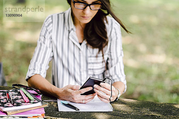 Frau mit Büchern auf dem Tisch mit Smartphone im Wald sitzend